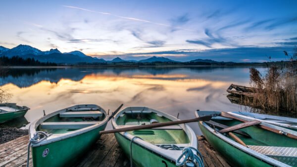 Roland Seichter Fotografie - Einzigartige Wandbilder - Landschaftfotografie - Abends am Hopfensee, im Vordergrund drei Ruderboote, im Hintergrund die Alpenkette