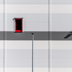 Roland Seichter Fotografie - Einzigartige Wandbilder - Minimalistische Fotografie - Eine grau-weiße Fassade mit einem rot gerahmten Fenster