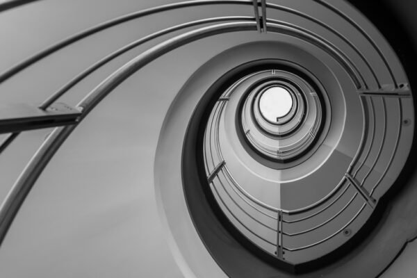 Roland Seichter Fotografie - Einzigartige Wandbilder - Architekturfotografie - Fotografie eines Treppenhauses von unten. Die Geometrie läuft auf einen außermittig gelegten Punkt zu. Schwarz/Weiß