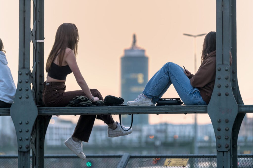 Roland Seichter Fotografie - Städtefotografie - München - Zwei junge Frauen sitzen auf den Eisenträgern des Hackerbrücke und schauen in den Abendhimmel
