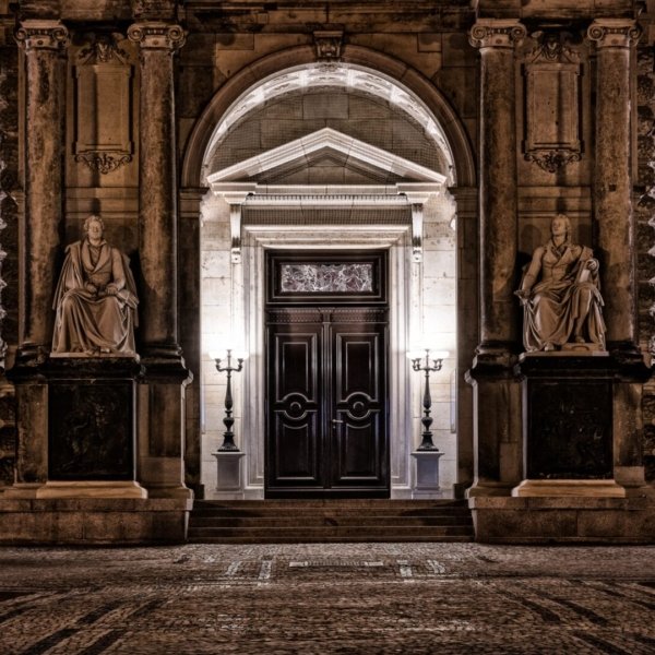 Eingang eines historischen Gebäudes mit Holztür, Statuen und Straßenlaternen.