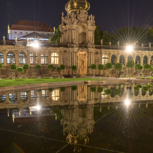 Barockgebäude mit goldener Krone bei Nacht, spiegelt sich in ruhigem Wasser, Sternlichter.