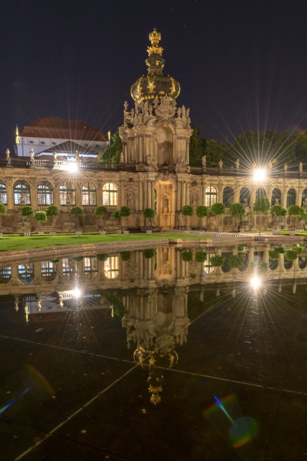 Barockgebäude mit goldener Krone bei Nacht, spiegelt sich in ruhigem Wasser, Sternlichter.