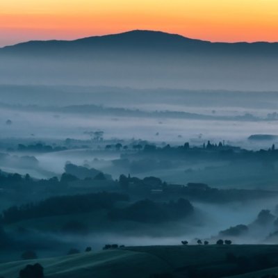 Roland Seichter Fotorgafie - Landschaftsfotografie - Morgenstimmung einer toskanischen Landschaft mit orange gefärbtem Himmel und einem dunklem Tal, in dem sich Nebel verfangen hat