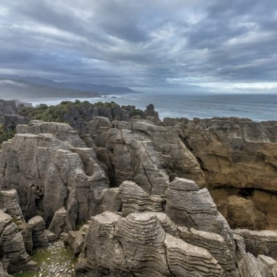 Küstenfelsformationen, geschichtet wie Pfannkuchen, vor bewölktem Himmel und Meer.