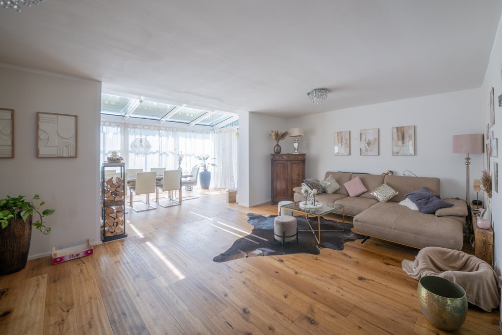 Roland Seichter Fotografie - Fotografische Dienstleistungen - Immobilienfotografie - Ansicht eines Wohnzimmers mit Sofa an der rechten Seite und Blick in den vom Raum abgetrennten Wintergarten mit Fensterfront und Esstisch im Raum
