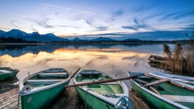 Roland Seichter Fotografie - Einzigartige Wandbilder - Landschaftfotografie - Abends am Hopfensee, im Vordergrund drei Ruderboote, im Hintergrund die Alpenkette