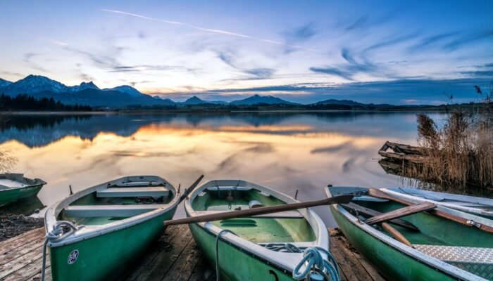 Roland Seichter Fotografie - Einzigartige Wandbilder - Landschaftfotografie - Abends am Hopfensee, im Vordergrund drei Ruderboote, im Hintergrund die Alpenkette