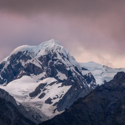 Schneebedeckter Berggipfel unter bewölktem Himmel mit Felsen und Gletschern.