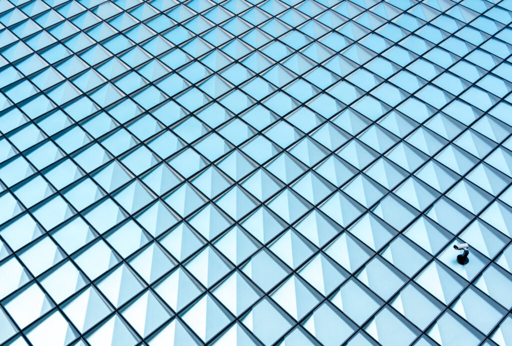 Roland Seichter Fotografie - Minimalistische Fotografie - Eine in Rauten strukturierte Glasfassade mit einer Überwachungskamera unten rechts