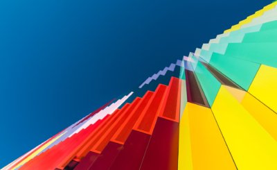 Roland Seichter Fotografie - Fotowettbewerbe - Blick auf eine bunte Fassade von unten. Die Bildkomposition platziert den Rand der Fassade und den blauen Himmel genau in die aufsteigende Diagonale