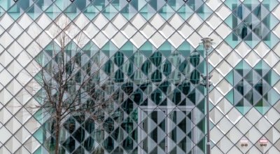 Roland Seichter Fotografie - Abstrakte Fotografie - BBild einer Glasfassade zusammengesetzt aus diagonal gestellten Glaselement. Im Vordergrund eine Laterne und ein entlaubter Baum
