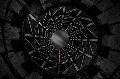 Roland Seichter Fotografie - Architekturfotografie - Der Blick in die kreisförmige Auffahrt eines Parkauses von unten. Alles ist sehr dunkel in SCchwarz/Weiß gehalten, lediglich ein Fallrohr hat seine rote Farbe behalten