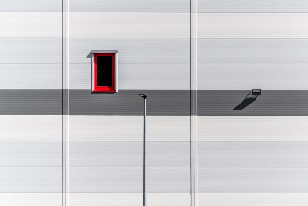 Roland Seichter Fotografie - Minimalistische Fotografie - Eine Hausfassade mit einem rot gerahmten Fenster und zwei Lampen