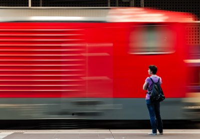Roland Seichter Fotografie - Fotowettbewerbe - Eine rote Lok fähr in den Bahnhof ein, das Bild ist bewegungsunscharf. Im Vordergrunf steht eine wartende Person