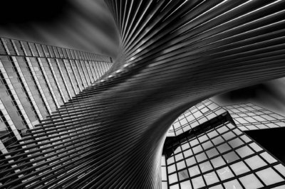 Roland Seichter Fotografie - Einzigartige Wandbilder - Städtefotografie - Blick von unten an Hochhäusern vorbei nach oben. Ein Kunstwerk bildet die Diagonale. Schwarz/Weiß