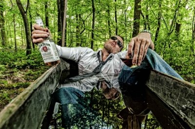 Roland Seichter Fotografie - Fotowettbewerbe - Ein junger Mann liegt angezogen in einer Badewanne im Wald und trinkt Whiskey