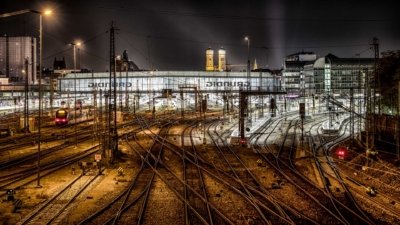 Roland Seichter Fotografie - Architekturfotografie - Ansicht des Münchner Haupbahnhofes von der hackerbrücke aus. Es ist Nacht, aber die Bahnhofshalle ist hell erleuchtet. Die Frauenkirche sieht man im Hintergrund