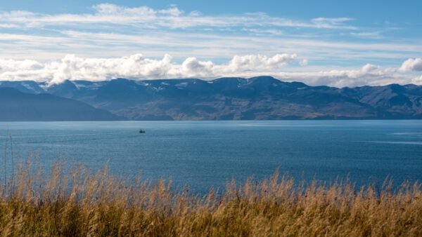 Roland Seichter Fotografie - Einzigartige Wandbilder - Fotografie mit Wasser - Eine ruhige Meeresbucht mit einer Hügelkette im Hintergrund. Blauer Himmel mit weißen Wolken