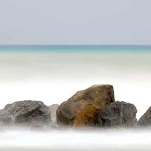 Roland Seichter Fotografie - Einzigartige Wandbilder - Fotografie mit Wasser - Große Steine am Strand, im Hintergrund das Meer in einer Langzeitbelichtung