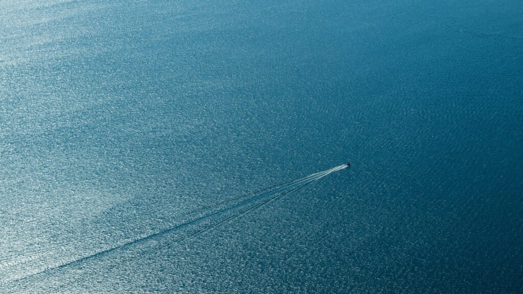 Roland Seichter Fotografie - Minimalistische Fotografie - Blick von weit oben auf einen See, ein kleines Boot erzeugt eine Spur