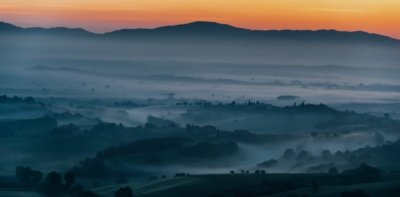 Roland Seichter Fotorgafie - Landschaftsfotografie - Morgenstimmung einer toskanischen Landschaft mit orange gefärbtem Himmel und einem dunklem Tal, in dem sich Nebel verfangen hat