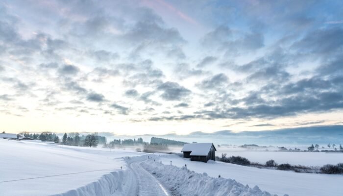 Roland Seichter Fotografie - Landschaftsfotografie - Blick in eine schneebedeckte Straße am Morgen, eine kleine Scheune im Vordergrund, kleine Wolken am Himmel