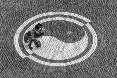 Roland Seichter Fotografie - Fotowettbewerbe - 2 Personen sitzen auf einer gepflasterten Fläche, das Muster des Pflasters zeigt das Yin-Yang Zeichen