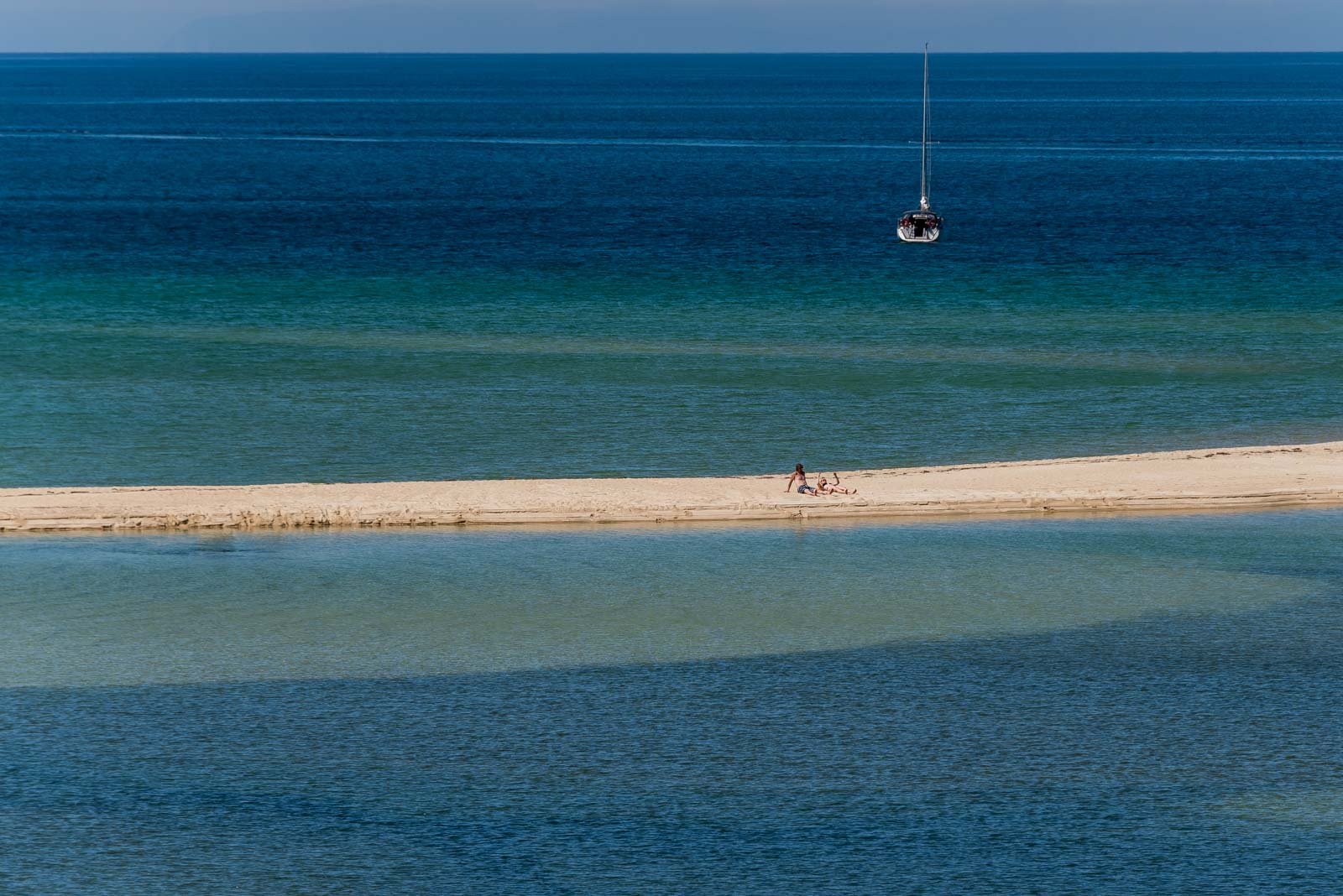 Segelboot vor der Küste des Abel Tasman Nationalparks mit Personen am Sandstrand.
