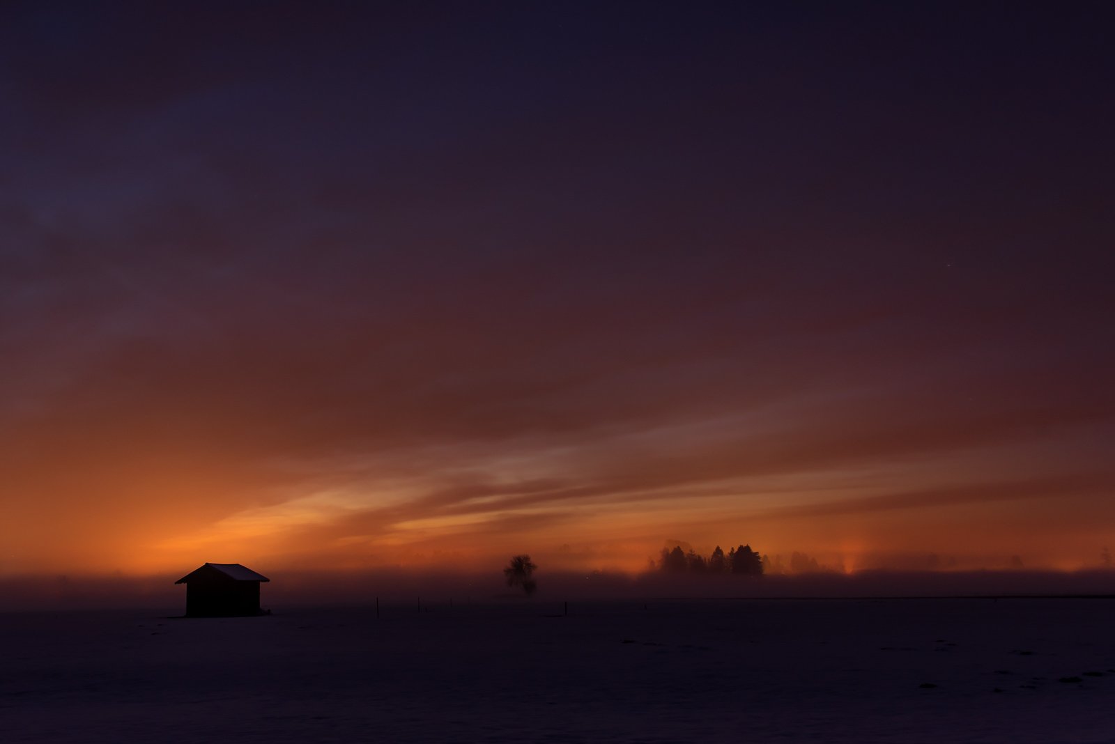 Stimmungsvolle Landschaftsaufnahme einer einsamen Hütte im Nebel bei Sonnenuntergang.