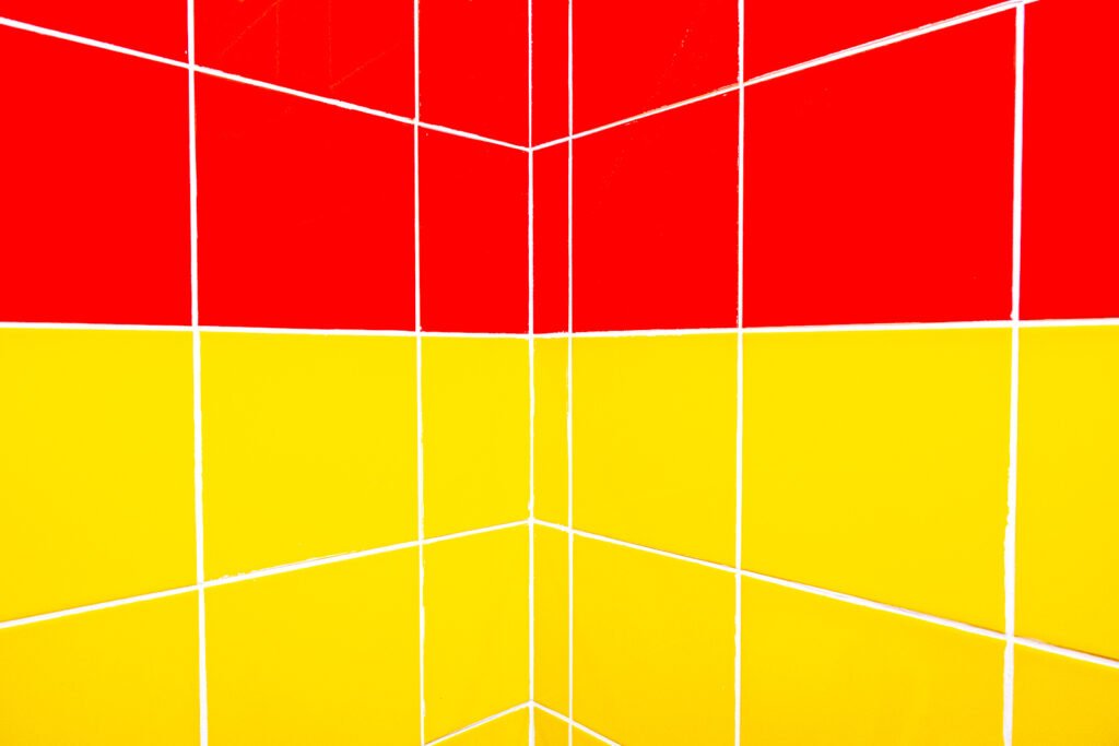 Minimalistische Architekturfotografie einer Mauerecke mit glänzenden roten und gelben quadratischen Fliesen und exakter Linienführung