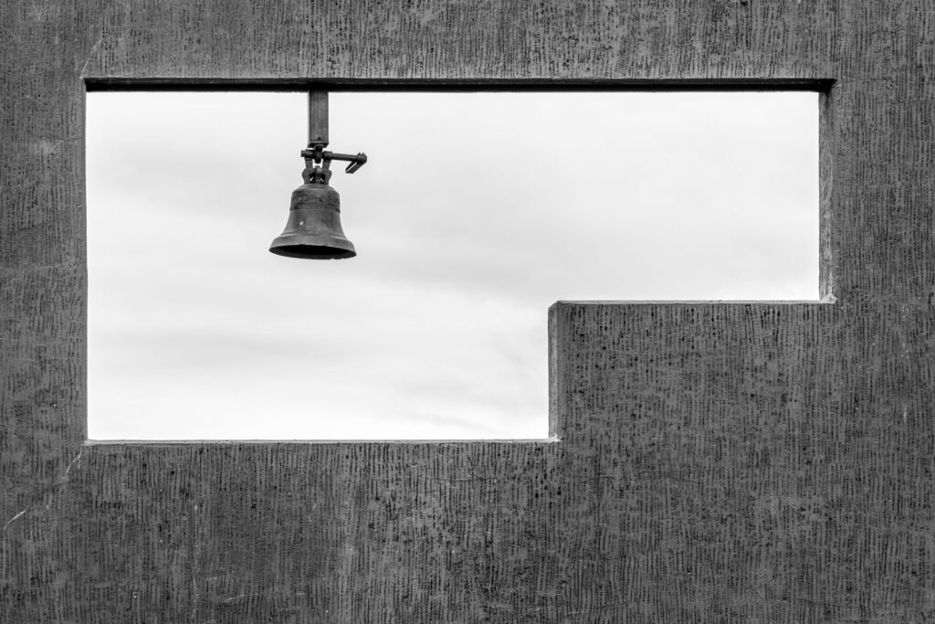 Minimalistische Schwarz-Weiß-Fotografie einer Glocke in einer rechteckigen Aussparung einer Betonwand