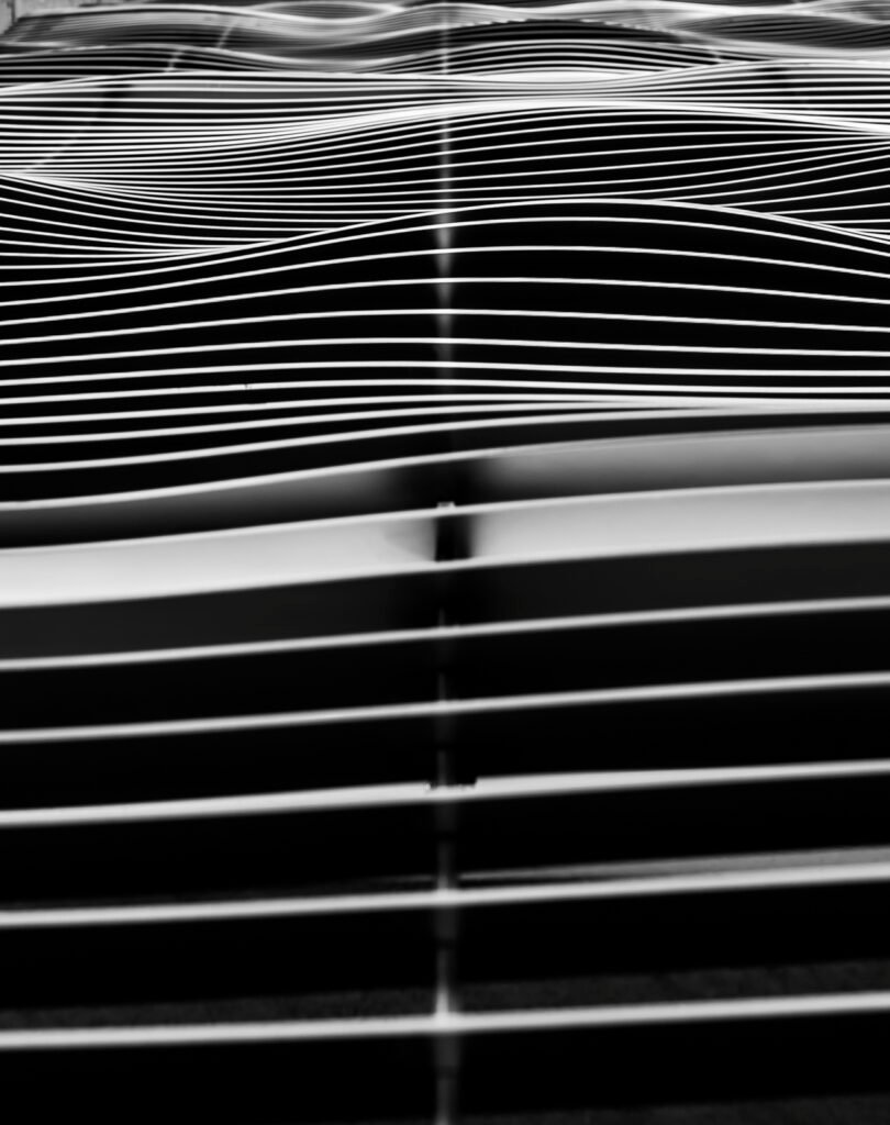 Abstrakte Schwarz-Weiß-Fotografie von wellenförmig angeordneten Metall-Lamellen an einer Fassade