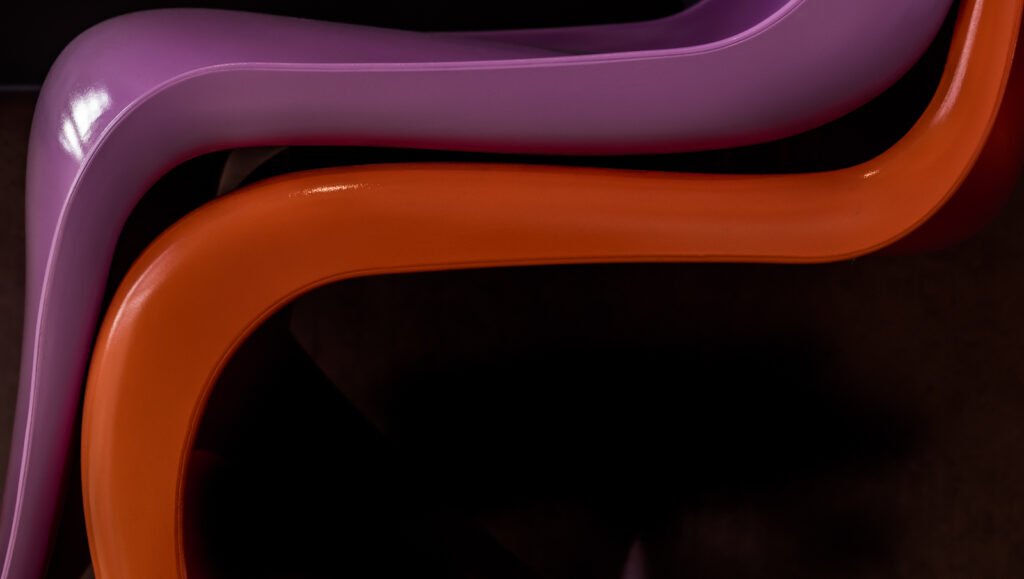 Abstrakte Detailaufnahme von zwei elegant geschwungenen Design-Elementen in glänzendem Lila und Orange vor dunklem Hintergrund