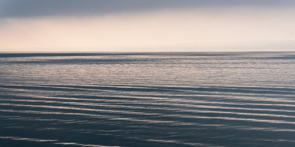 Minimalistische Fotografie einer ruhigen Wasserfläche mit sanften Wellenstrukturen in Pastelltönen