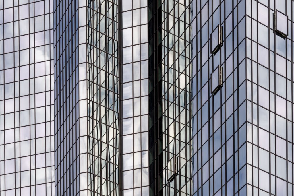 Abstrakte Fotografie einer modernen Glasfassade mit strengem Fensterraster und Spiegelungen urbaner Strukturen
