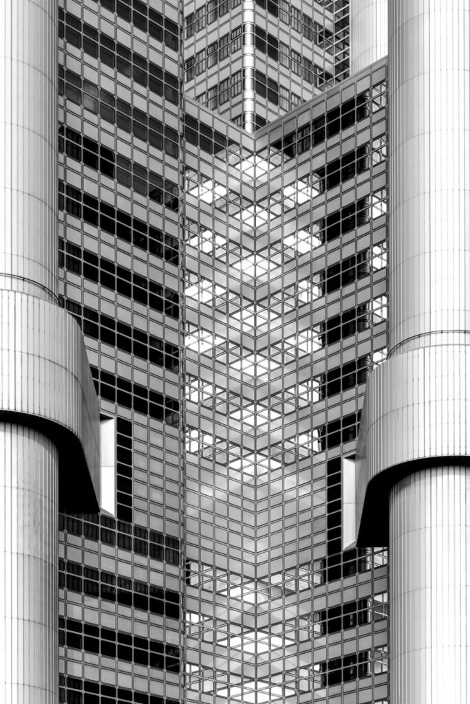 Abstrakte Schwarz-weiß-Fotografie einer modernen Hochhausfassade mit symmetrischen Säulenstrukturen und geometrischem Fensterraster