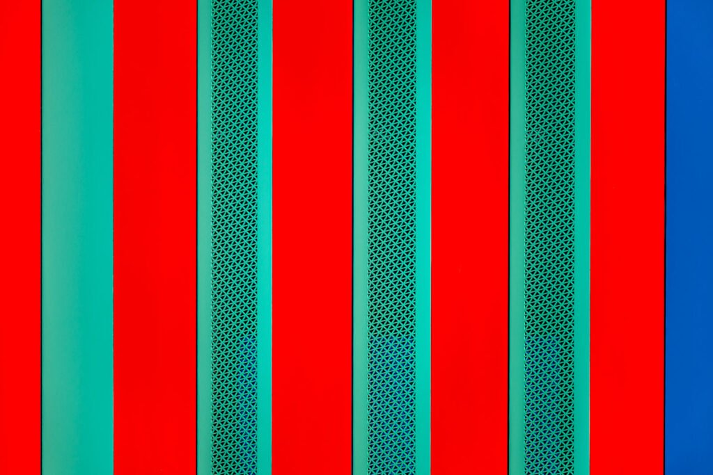 Abstrakte Architekturfotografie mit vertikalen roten und grünen Streifen sowie perforierten Metallelementen in exakter geometrischer Anordnung
