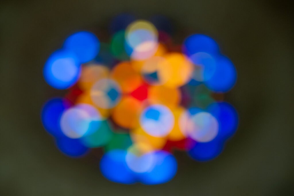 Abstrakte Fotografie von bunten, kreisförmigen Lichtpunkten (Bokeh) in Blau, Gelb und Rot vor dunklem Hintergrund