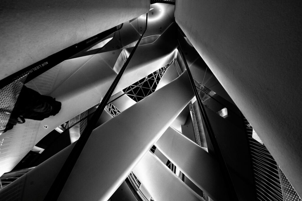 Abstrakte Schwarz-Weiß-Fotografie der Unterseite von zwei parallel laufenden Rolltreppen mit rhythmischer Linienstruktur