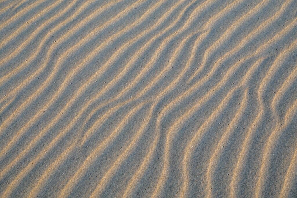 Abstrakte Fotokunst von rhythmischen Wellenstrukturen im Sand einer Düne bei sanftem Seitenlicht
