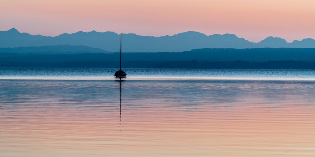 Minimalistische Landschaftsfotografie am Ammersee: Segelschiff im Abendrot vor der Alpenkette.