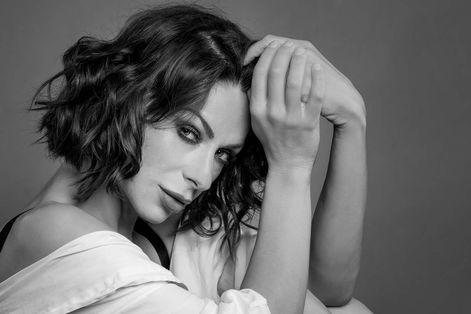 Ausdrucksstarkes Schwarz-Weiß-Porträt einer Frau mit dunklen, lockigen Haaren in einer nachdenklichen Pose.