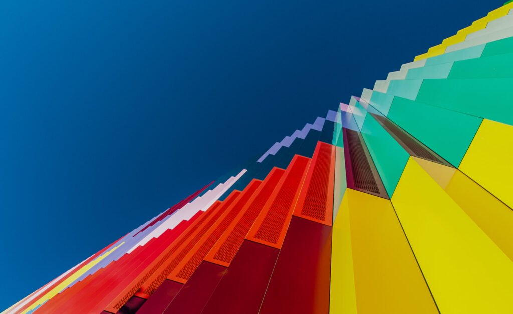 Abstrakte Untersicht einer farbenfroh gestalteten Gebäudefassade in Spektralfarben vor tiefblauem Himmel.