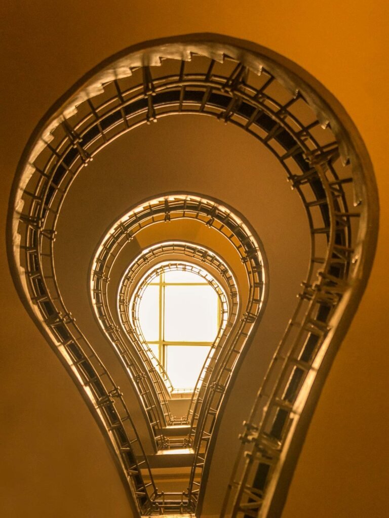 Blick von unten in das berühmte kubistische Treppenhaus des Café Orient in Prag in warmen Goldtönen.