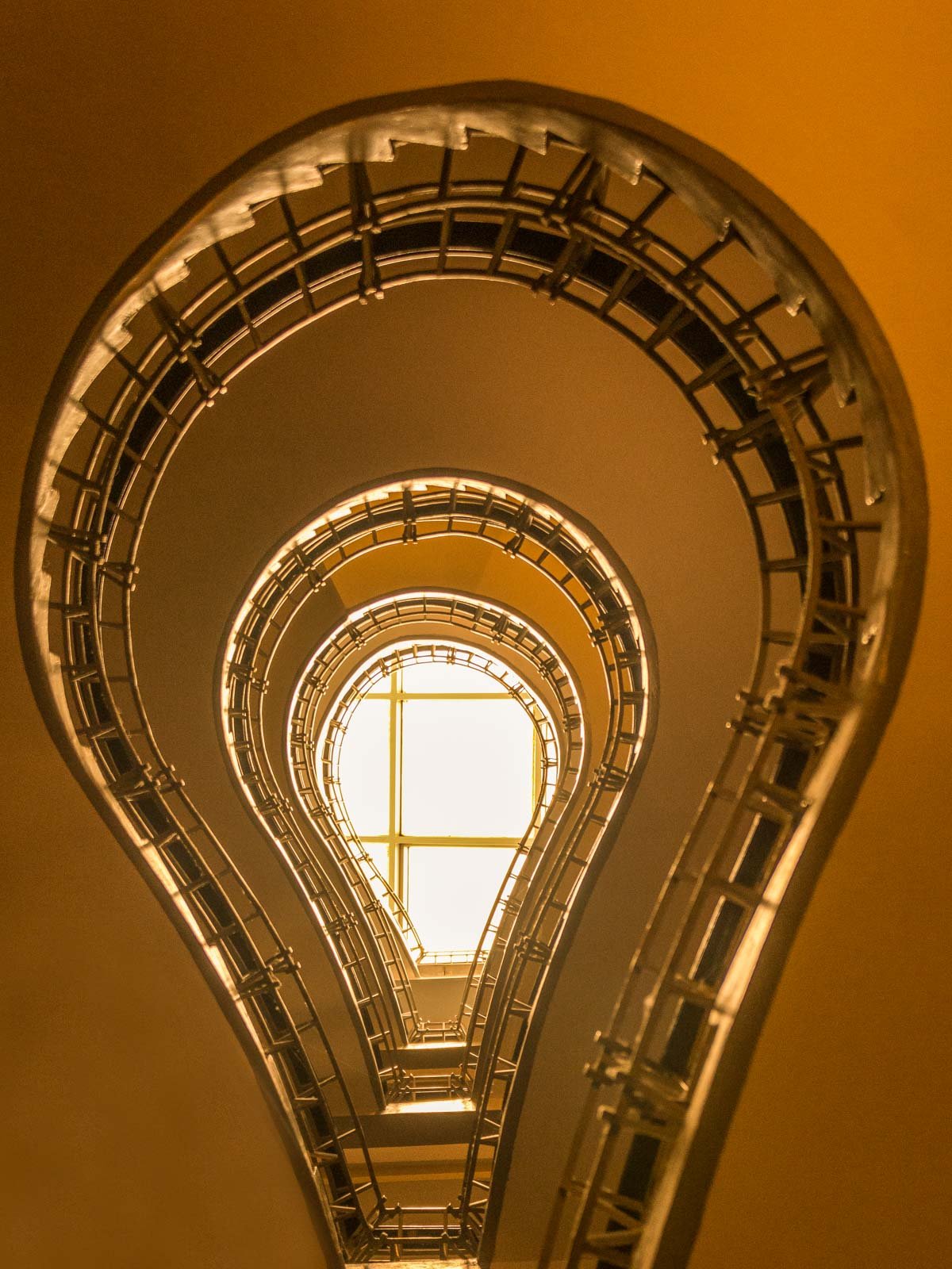 Blick von unten in das berühmte kubistische Treppenhaus des Café Orient in Prag in warmen Goldtönen.