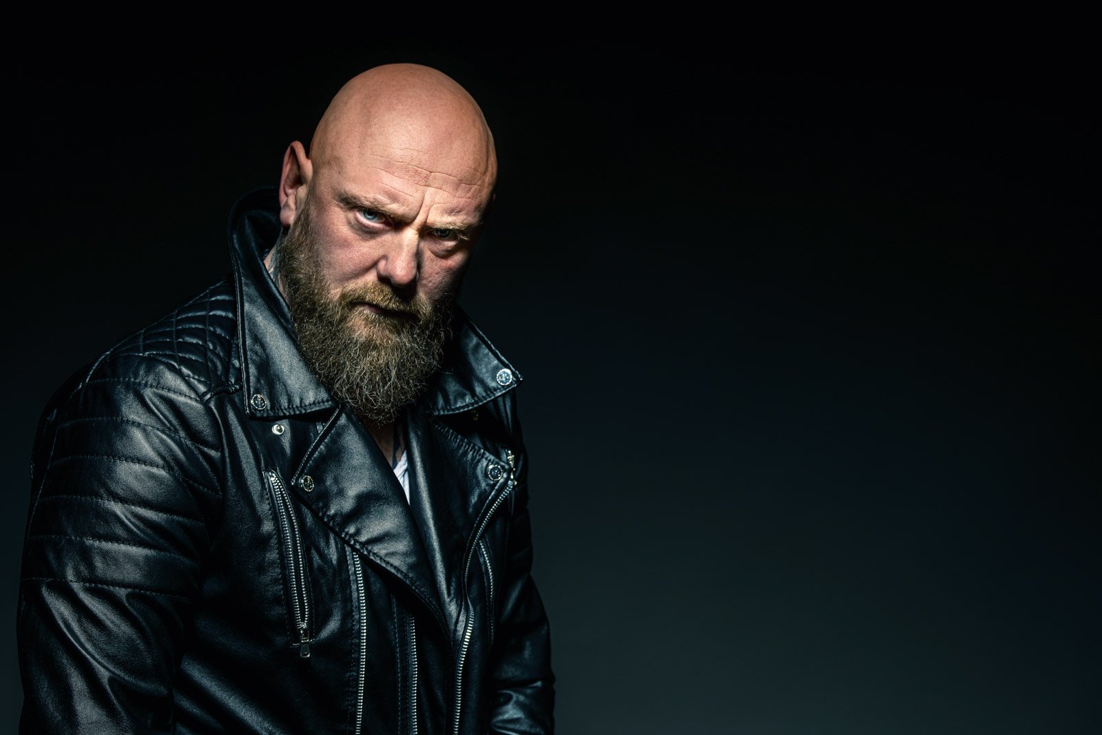 Charakterporträt eines Mannes mit Bart und Lederjacke, der mit intensivem Blick direkt in die Kamera schaut.
