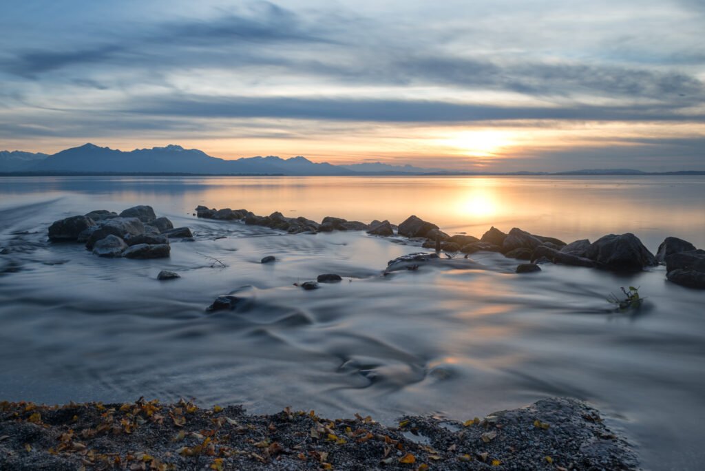 Chiemsee Landschaftsfotografie: Abendstimmung mit Bergen und Spiegelung in Langzeitbelichtung.