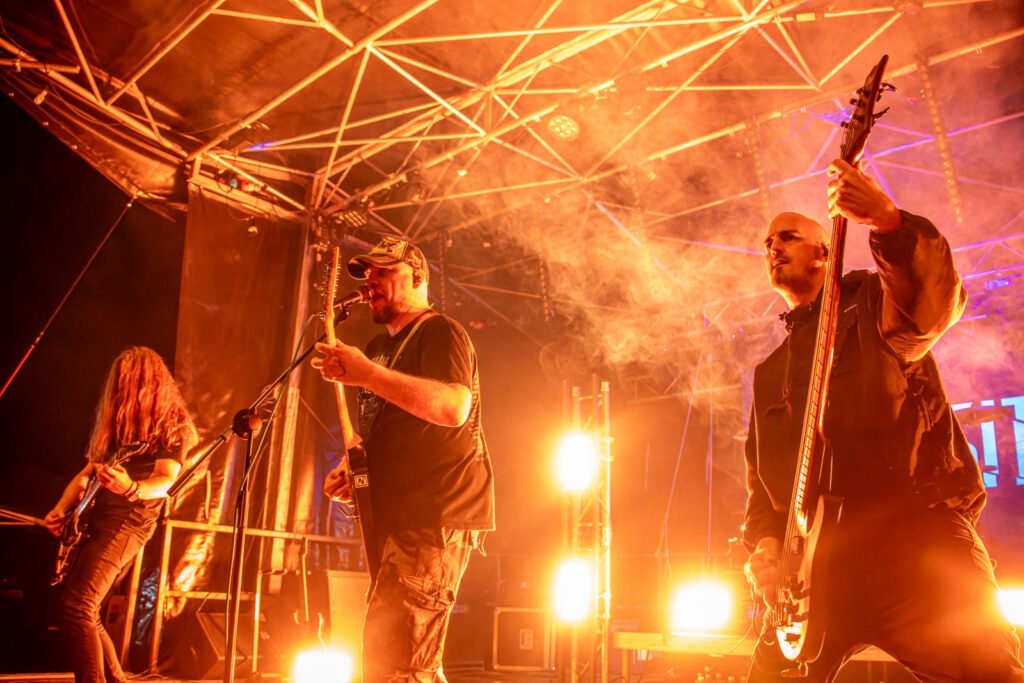Atmosphärische Live-Aufnahme der Band in warmem, orangem Gegenlicht, Rauch und Silhouetten erzeugend. Foto: Roland Seichter.
