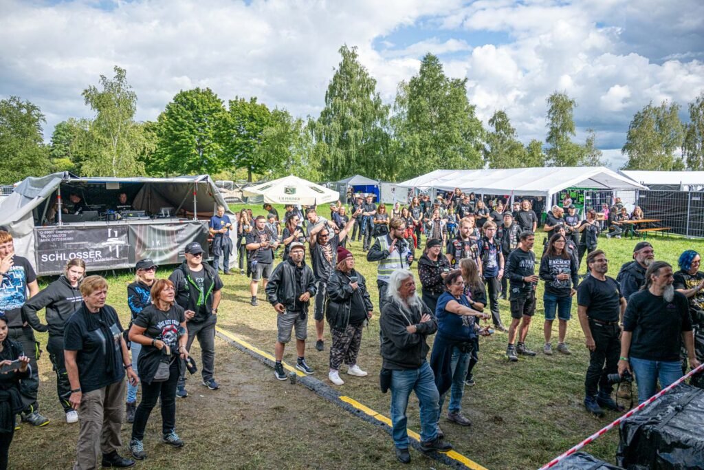 Weitwinkelaufnahme der feiernden Festival-Crowd auf grünem Gelände, die einzigartige Stimmung im Wald einfangend.